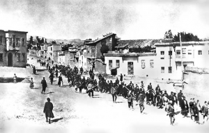 Armed Turkish soldiers march Armenians to prison in Mezireh, April 1915. Image in public domain.